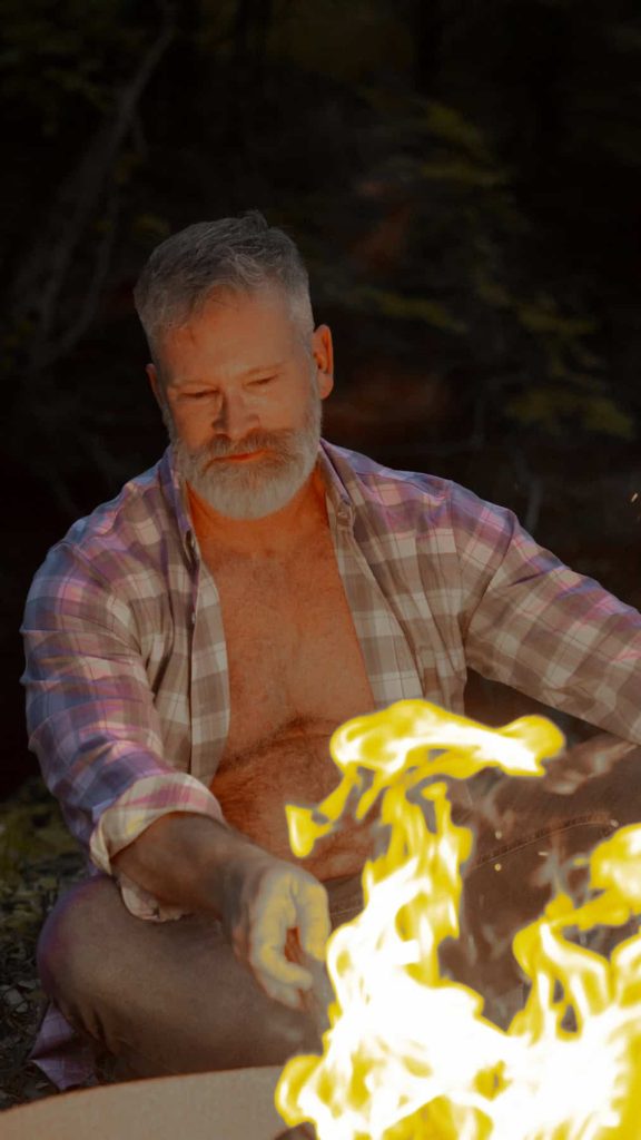Manly man outdoors in the country by a fire.
